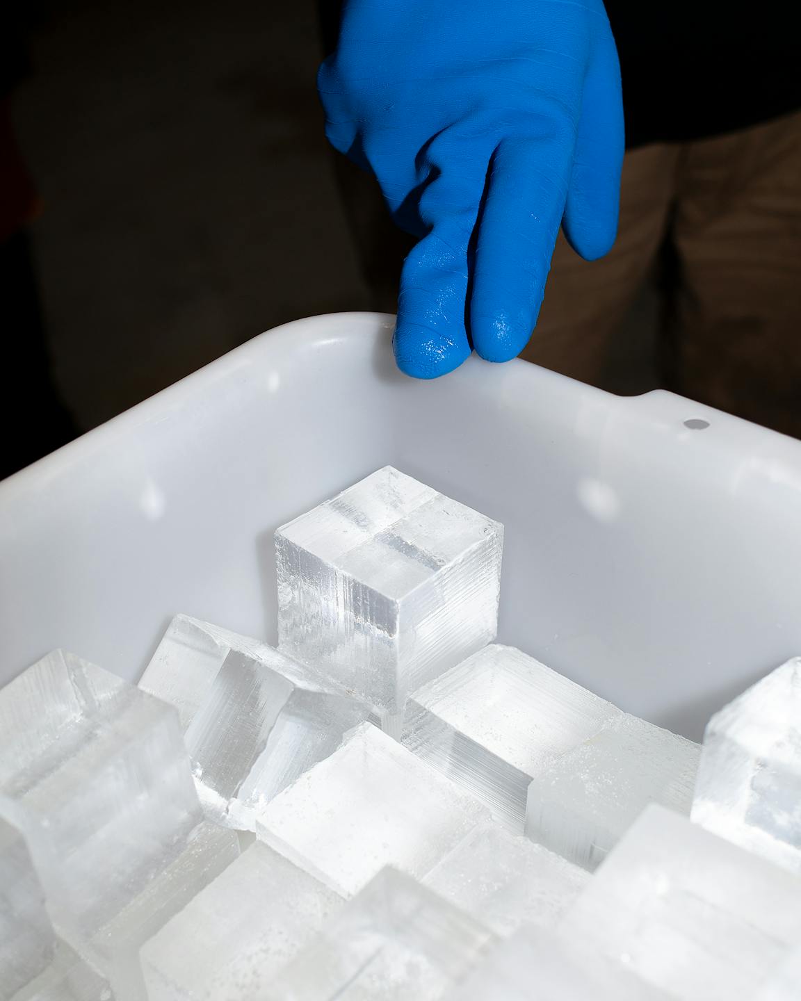A gloved hand reaches into a tub of perfectly cubed ice.